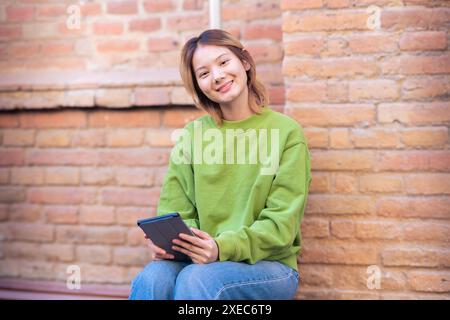 Jeune femme asiatique souriante assise surfant sur Internet sur une tablette numérique. Banque D'Images