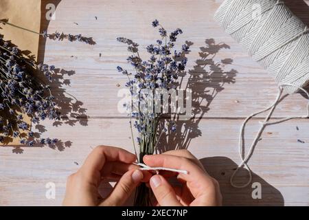 Vue de dessus plat de processus de fabrication de bouquets de fleurs de lavande séchées. Corde de coton, ciseaux. Femelle faire bouquet d'herbes maison Banque D'Images