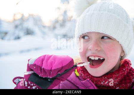 Jolie petite fille tout en mangeant de l'icicle le beau jour d'hiver Banque D'Images