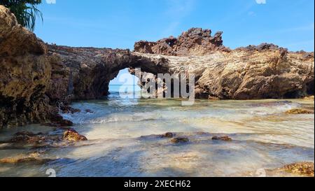 Une plage rocheuse avec une petite arche debout au milieu, encadrant la vue panoramique sur le paysage marin environnant Banque D'Images