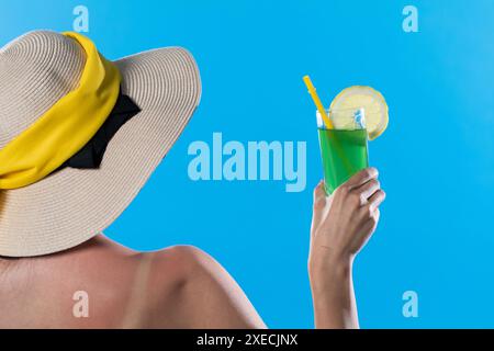 L'adolescente a tourné le dos avec un chapeau sur la tête et la main tient un verre avec une boisson fraîche par une journée ensoleillée. Banque D'Images