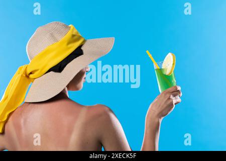 L'adolescente a tourné le dos avec un chapeau sur la tête et la main tient un verre avec une boisson fraîche par une journée ensoleillée. Banque D'Images