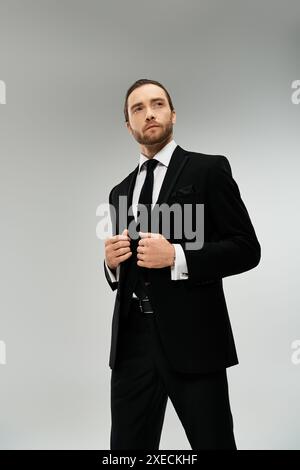 Un homme d'affaires élégant et barbu portant un costume et une cravate prend une pose confiante sur un fond gris de studio. Banque D'Images