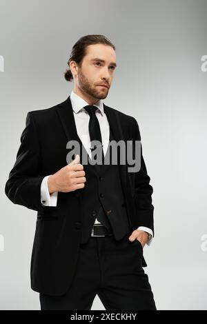 Un homme d'affaires barbu et beau, vêtu d'un costume et d'une cravate, prend une pose confiante sur un fond gris de studio. Banque D'Images