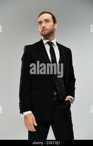 Bel homme d'affaires barbu dans un costume et une cravate frappant une pose confiante sur un fond gris de studio. Banque D'Images