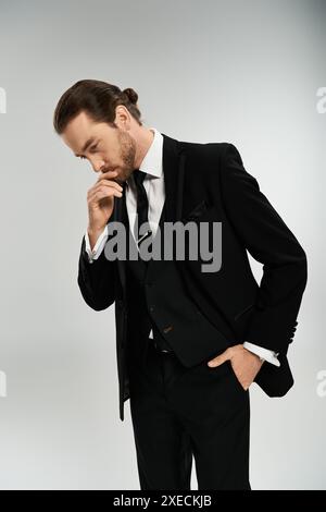 Un homme d'affaires barbu dans un costume de dapper prend une pose confiante sur un fond gris de studio. Banque D'Images