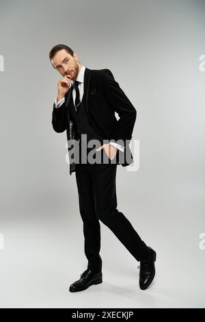 Un bel homme d'affaires barbu pose gracieusement dans un smoking sur fond de studio gris. Banque D'Images