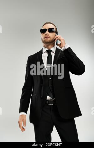 Homme d'affaires barbu dans un costume élégant et des lunettes de soleil conversant sur un téléphone portable, exsudant la confiance et le professionnalisme. Banque D'Images