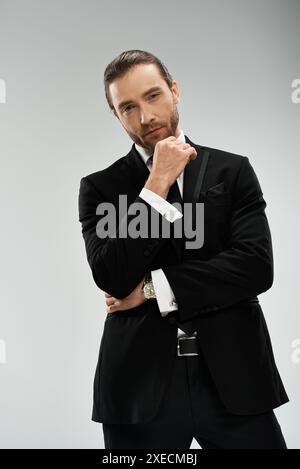 Un homme d'affaires barbu dans un costume élégant et cravate frappe une pose confiante sur un fond gris de studio. Banque D'Images