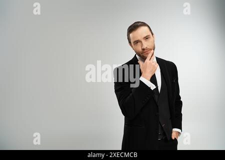 Un bel homme d'affaires barbu vêtu d'un costume prend la pose sur un fond gris dans un cadre de studio. Banque D'Images