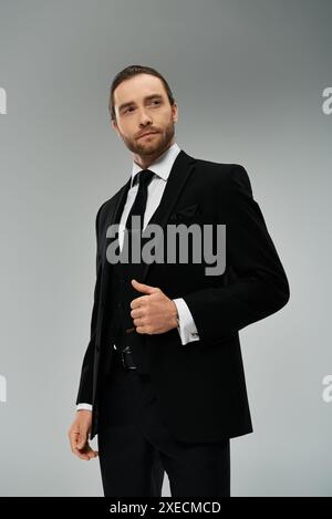 Un bel homme d'affaires barbu en costume et cravate frappe une pose confiante dans un studio sur un fond gris. Banque D'Images