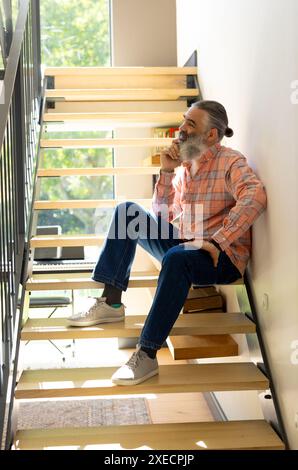 Assis sur les escaliers, homme senior dans des vêtements décontractés pensant et se relaxant à la maison Banque D'Images