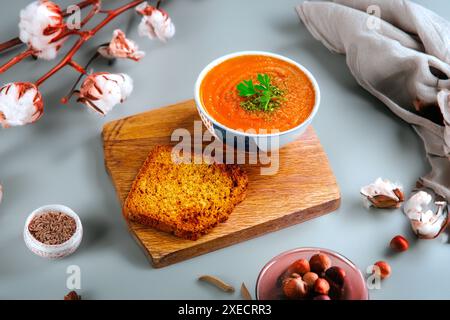 Un bol de soupe crémeuse à la tomate garni de persil, accompagné d'une tranche de pain grillé sur une planche de bois. Banque D'Images