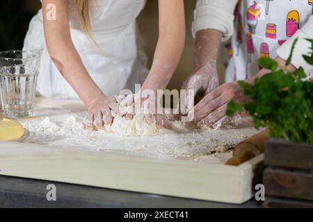 Gros plan. Dans l'une des dernières étapes, la mère et la fille pétrissent et pétrissent un gâteau qui servira de gâteau à pizza. Mère an Banque D'Images