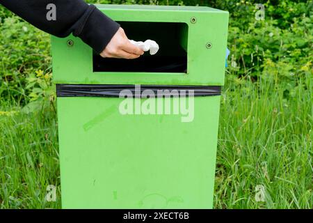 Bras jeter les déchets dans la poubelle dans un centre de loisirs en plein air. Herbe et buissons derrière la poubelle. Notion de considération et de bienveillance. Banque D'Images