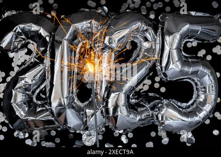 Bonne année 2025 ballons métalliques avec des confettis et des feux d'artifice scintillants Bengale sur fond noir foncé. Carte de voeux Banque D'Images