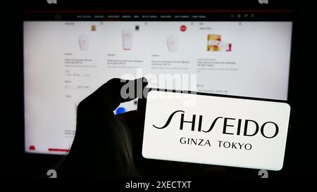 Personne tenant le téléphone portable avec le logo de la société cosmétique japonaise Shiseido Co. Ltd devant la page Web de l'entreprise. Concentrez-vous sur l'affichage du téléphone. Banque D'Images
