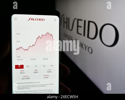 Personne tenant le téléphone portable avec la page Web de la société cosmétique japonaise Shiseido Co. Ltd devant le logo. Concentrez-vous sur le centre de l'écran du téléphone. Banque D'Images