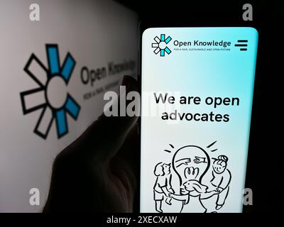 Personne tenant un téléphone portable avec le site Web de l'organisation mondiale Open Knowledge Foundation (OKF) devant le logo. Concentrez-vous sur le centre de l'écran du téléphone. Banque D'Images