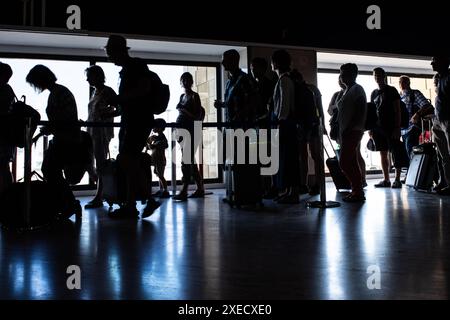 Silhouettes de passagers debout dans la file à l'intérieur de l'Aeropuerto de Sevilla, España, avec des bagages et des bagages à main, attendant leur appel d'embarquement. Banque D'Images