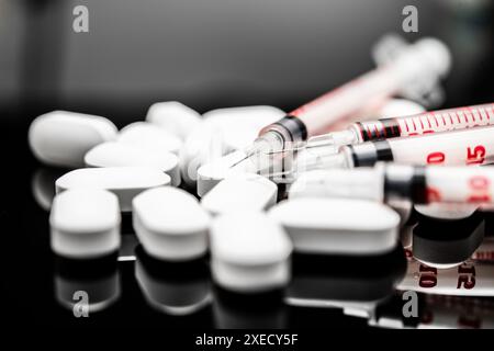 Vue rapprochée des pilules de médicaments blancs et des seringues médicales sur une surface réfléchissante, des médicaments sur ordonnance, des opioïdes sur ordonnance, du fentanyl Banque D'Images