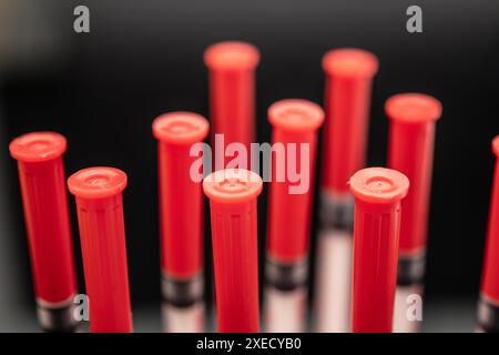 Gros plan de plusieurs tubes à essai en plastique rouge dans un cadre de laboratoire sombre, équipement médical ciblé et détaillé et injection d'insuline Banque D'Images