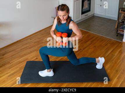 Femme athlétique faisant de l'entraînement de force avec deux haltères à la maison. Banque D'Images