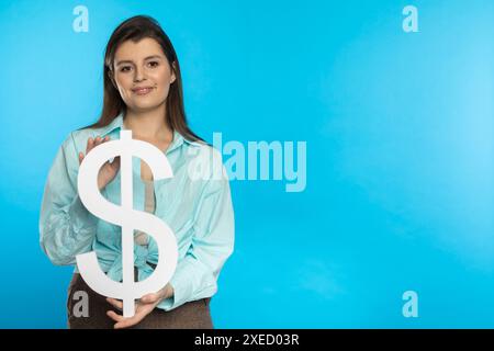 La fille tient un grand symbole du dollar dans ses mains. La forme de la monnaie américaine. Symbole de la finance et des flux de trésorerie dans l'économie Banque D'Images