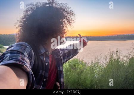 Personne aux cheveux bouclés profitant d'un coucher de soleil au bord du lac Banque D'Images