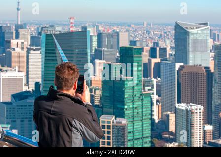 Homme prenant une photo par téléphone à la terrasse d'observation devant les gratte-ciel pendant la journée ensoleillée à Tokyo Banque D'Images