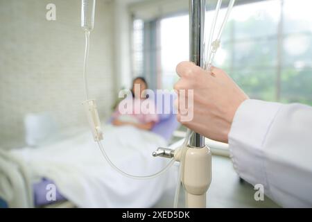 Médecin féminin avec équipement IV donnera des liquides IV et examinera les patients couchés dans les lits d'hôpital Banque D'Images