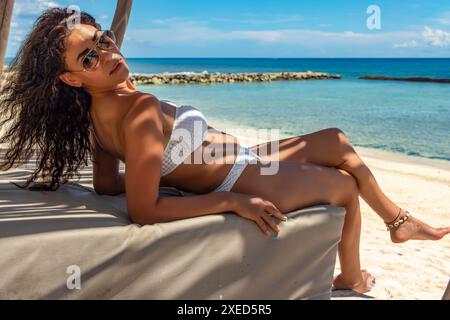 Image d'une femme se relaxant dans un bikini sur un lit balinais, ses cheveux soufflés par le vent et son expression paisible capturent l'essence du paradis tropical et d'une sere Banque D'Images