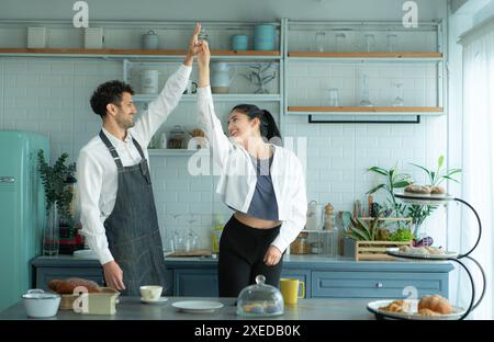 Un mari porte un tablier en cuisinant le dîner avec sa femme. Il dansait joyeusement avant d'entrer dans la cuisine pour cuisiner. Banque D'Images