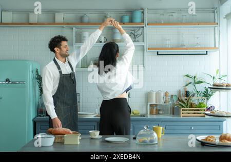 Un mari porte un tablier en cuisinant le dîner avec sa femme. Il dansait joyeusement avant d'entrer dans la cuisine pour cuisiner. Banque D'Images