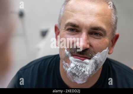 Un homme d'âge moyen qui se rasse sa barbe dans la salle de bains Banque D'Images