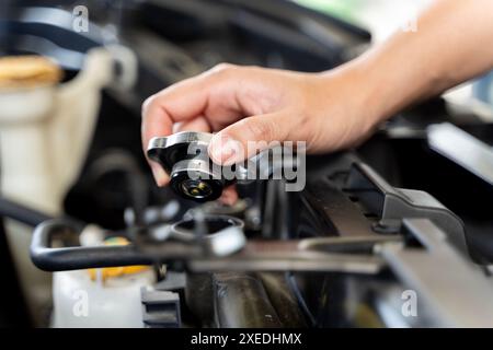 Une personne tient un entonnoir et verse du liquide de refroidissement dans le radiateur d'une voiture et ils se tiennent devant une voiture. Le capot de la voiture est ouvert, et Banque D'Images