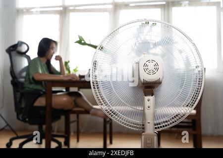 Été ensoleillé devant le ventilateur de travail, souffrant de la chaleur estivale. Malheureuse femme asiatique assise devant un ventilateur au travail souffrant de chaleur en M. Banque D'Images
