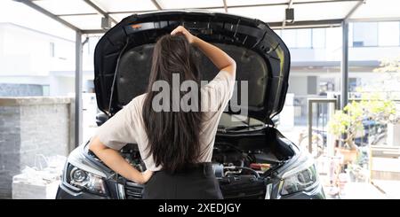 Femme debout devant sa voiture. Elle a une expression d'inquiétude sur son visage et regarde sa voiture avec soin. Il est possible que sa voiture ait b Banque D'Images