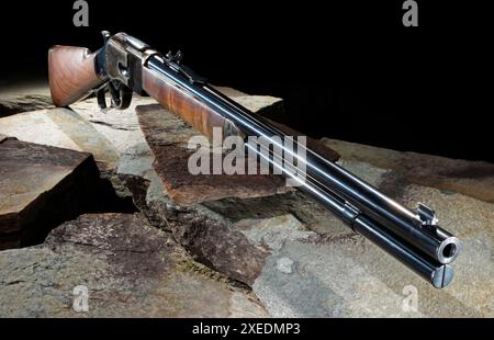Fusil qui est une action de levier avec un stock de bois et acier bleui sur de grandes pierres plates avec un fond noir. Banque D'Images