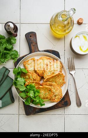 Beignets de courgettes végétales avec poivre à la crème sure et huile d'olive servis sur une assiette rustique sur un vieux fond de table en carreaux craquelés. Végétarien sain fo Banque D'Images