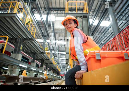 Portrait de femme technicien avec boîte à outils, assis sur un piédestal en ciment devant les voies de train électrique dans le skytrain R Banque D'Images