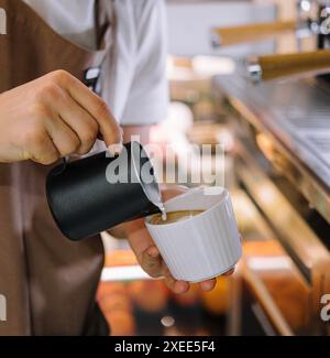 Le barista verse du lait dans le café Banque D'Images