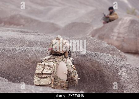 Un soldat taliban se tient debout avec une mitrailleuse, se rend aux soldats alliés, dans le champ de bataille du terrain de montagne du désert Banque D'Images