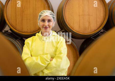 Viticulteur féminin souriant en uniforme jaune debout dans la cave de la cave Banque D'Images