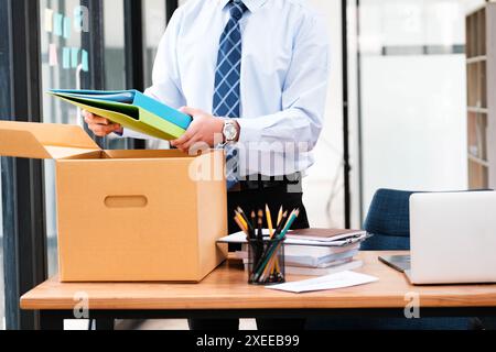 Un homme en costume ouvre une boîte en carton sur un bureau Banque D'Images