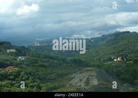 Une vue pittoresque sur les collines vallonnées couvertes de verdure luxuriante avec un petit village niché au loin sous un ciel nuageux. Banque D'Images