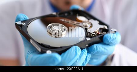 Un réparateur d'hommes portant des gants bleu est la tenue d'un disque dur d'ordinateur ou ordinateur portable dans les mains. Effectue le diagnostic et effectue les réparations urgentes Banque D'Images