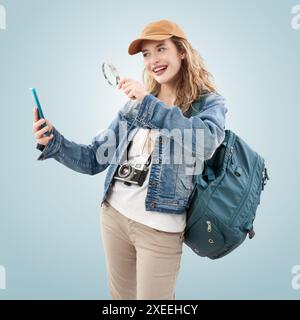 Voyager heureux jeune femme souriante routard touriste recherchant sur téléphone portable les meilleures offres et offres de voyage avec la loupe. Concept de s Banque D'Images