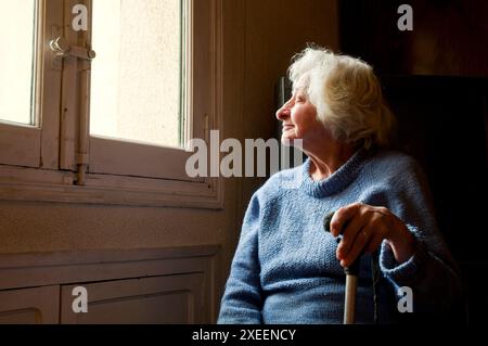 Portrait de vieille femme à la maison, souriant et regardant la fenêtre. Banque D'Images