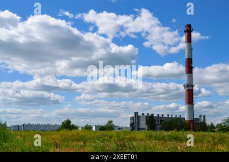 Grande cheminée rayée rouge et blanche d'une chaufferie sur fond de nuages blancs dans le ciel bleu Banque D'Images